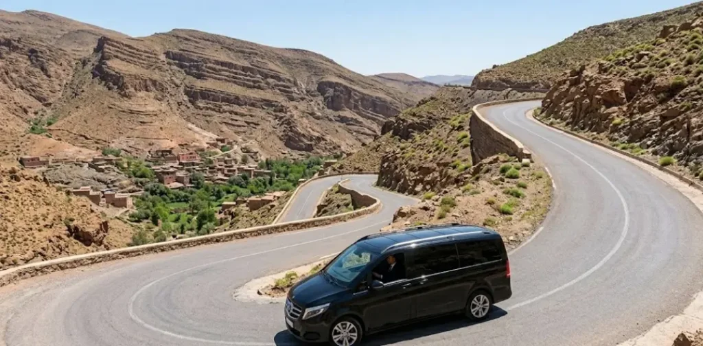 An executive black Mercedes-Benz V-Class minivan navigating a sharp hairpin curve on the modern asphalt roads of the High Atlas Mountains during a private excursion from Marrakech.
